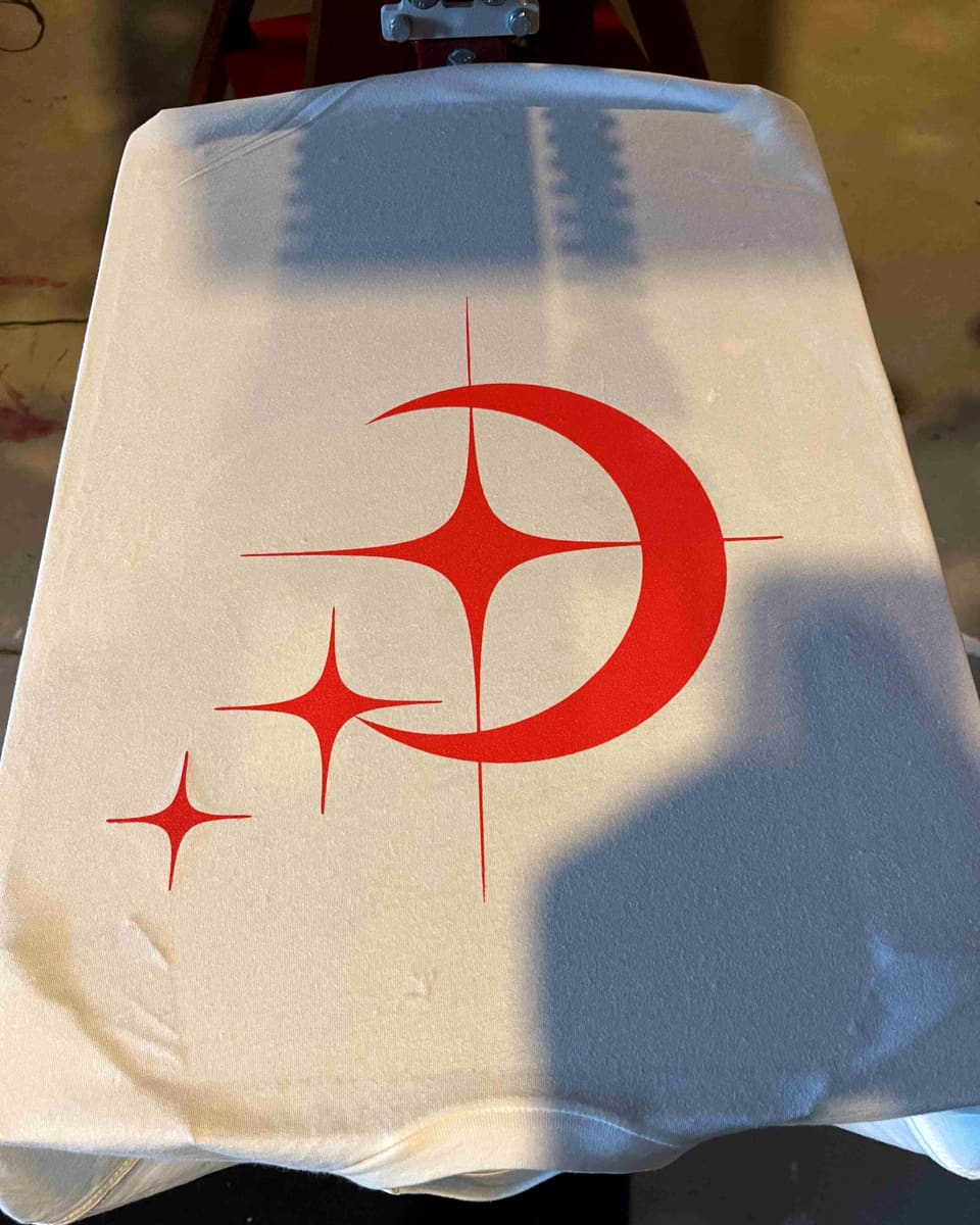 A white tee on the press platen with a freshly printed red crescent-and-stars design.