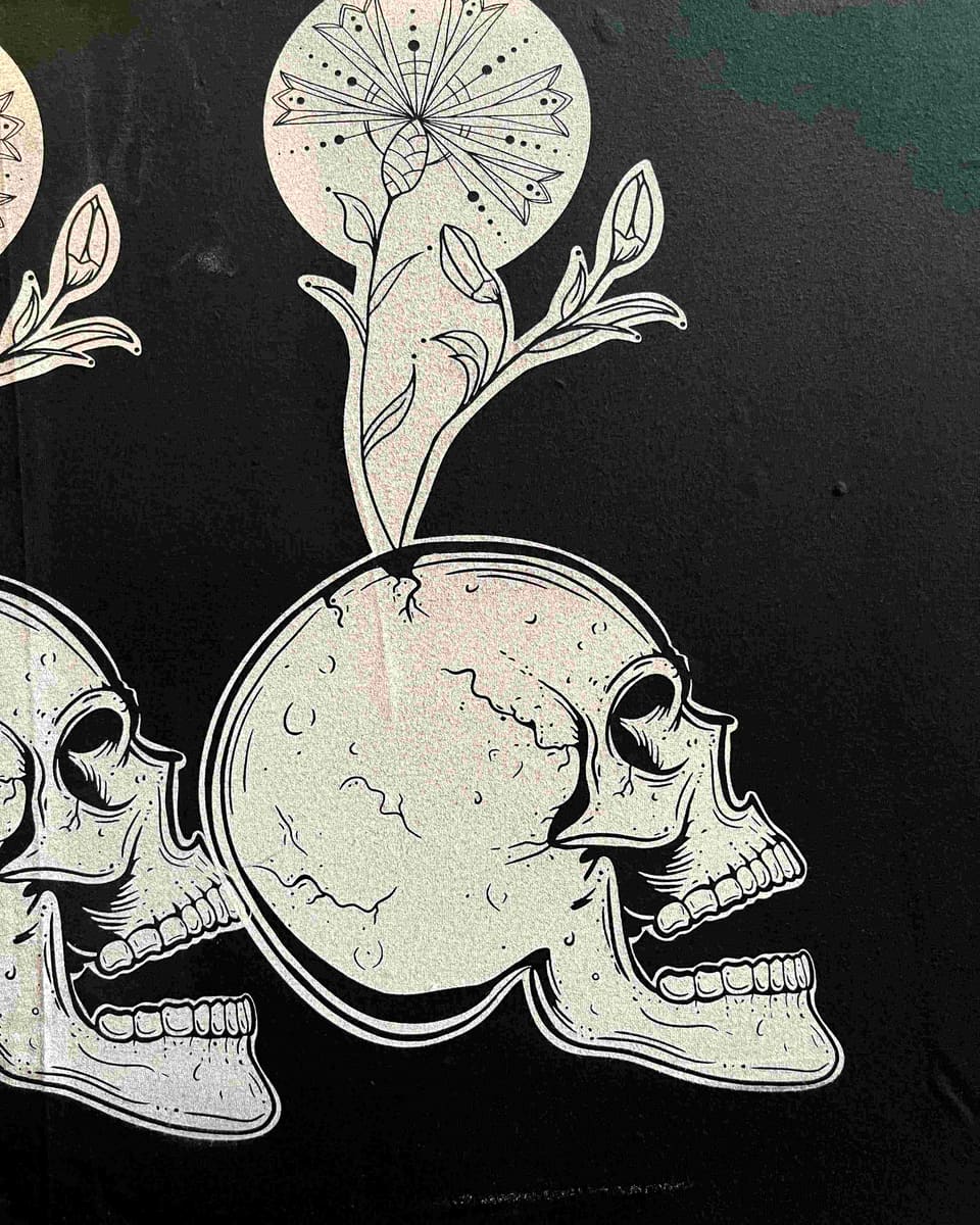 Close-up of skull-and-flower line artwork printed in a pale shimmering ink on black fabric.