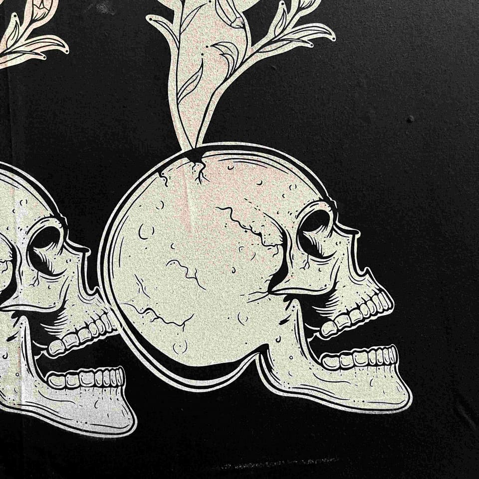 Close-up of skull-and-flower line artwork printed in a pale shimmering ink on black fabric.