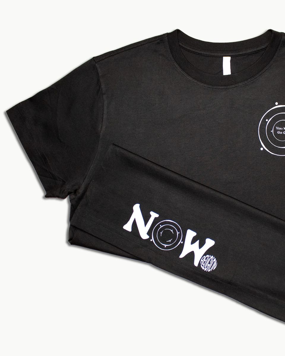 Two black tees laid over each other showing a chest print and a 'NOW' hem print in white.